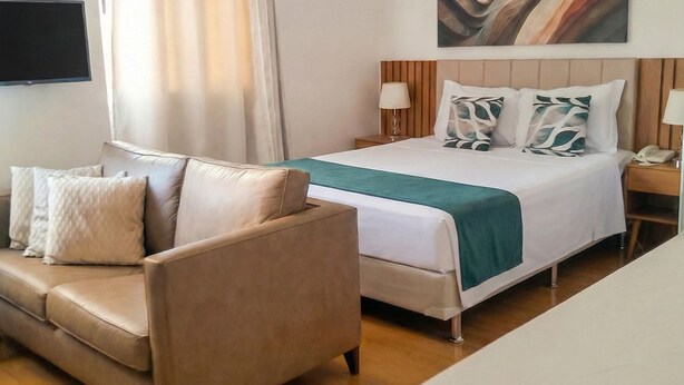 A hotel room with a bed, a sofa, a TV, and a painting on the wall. - Lindo Apto algumas quadras da Paulista (São Paulo)