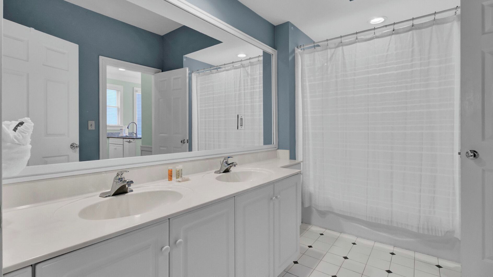 A bathroom with two sinks, a large mirror, a shower curtain, and a tiled floor.