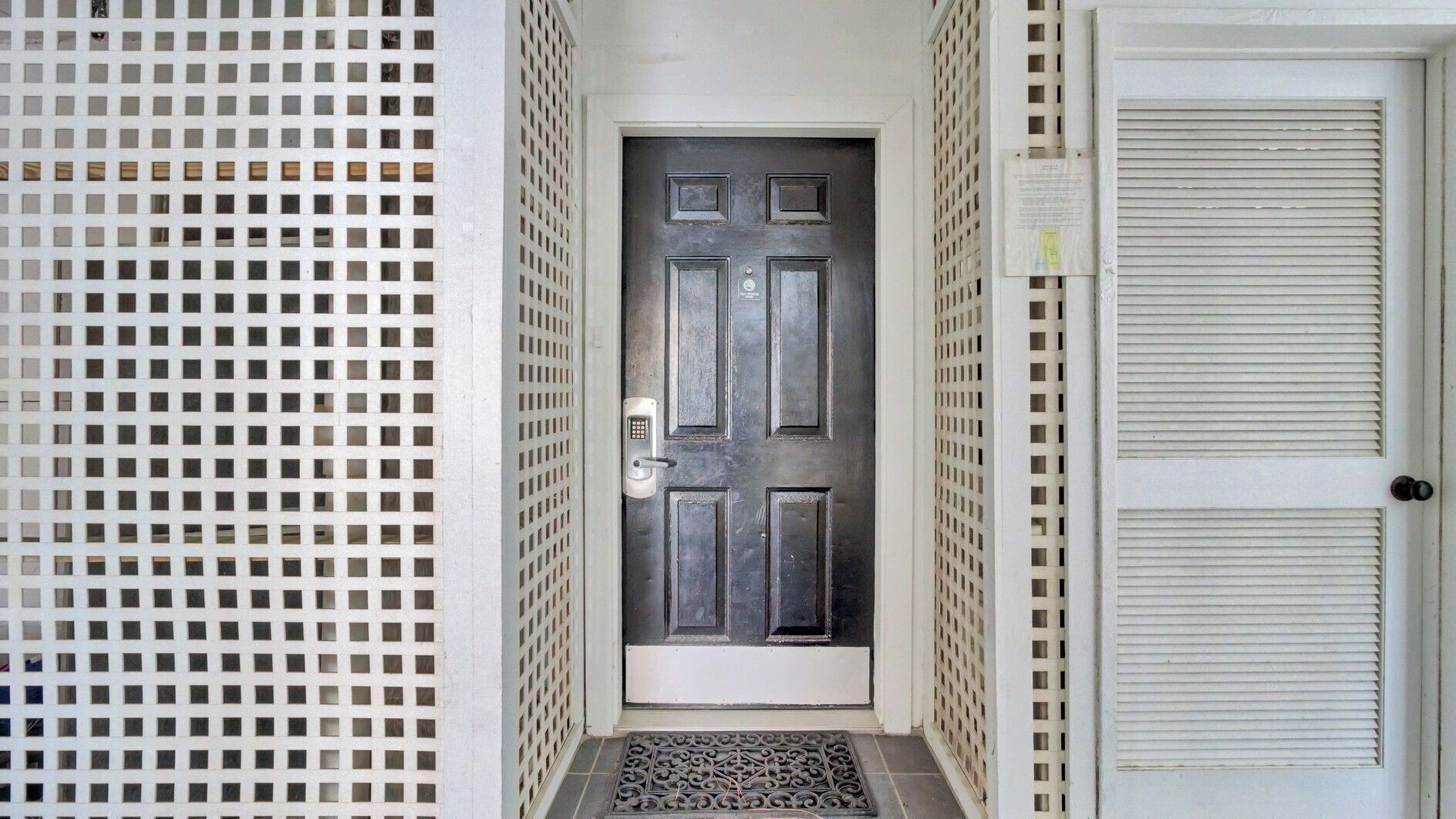A narrow hallway with a dark door, a metal gate, and a white door with a window.