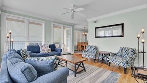A living room with a sofa, armchairs, a coffee table, and a dining area with chairs. - 110 Grand Pavilion by Avantstay Direct Access To Grand Pavilion Boardwalk (Isle of Palms)