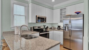 A kitchen with white cabinets, a stainless steel refrigerator, a microwave, a stove, and a sink. - 110 Grand Pavilion by Avantstay Direct Access To Grand Pavilion Boardwalk (Isle of Palms)