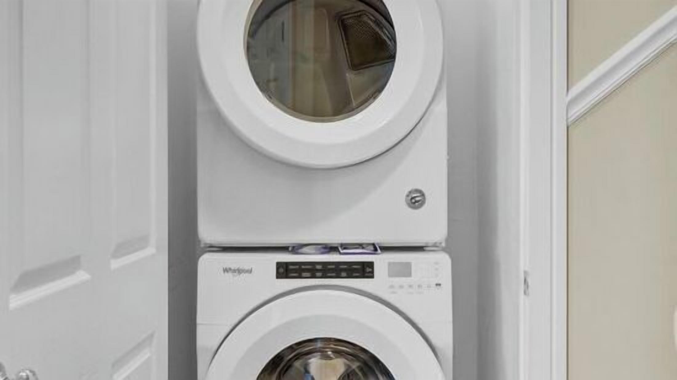 A stacked washer and dryer unit in a room with a plain wall and a door.