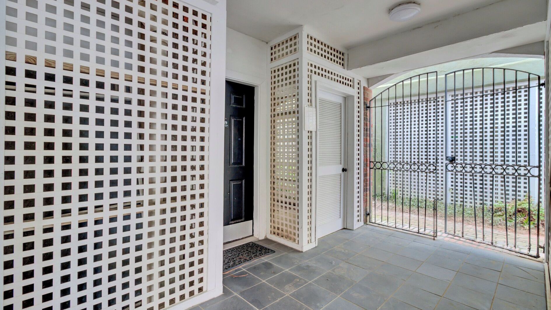 Uma entrada de edifício com porta de treliça branca, porta preta e portão de metal.