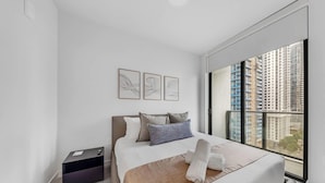 Een moderne hotelkamer met een groot bed, een nachtkastje, een klein bureau en een raam met uitzicht op de stad.
