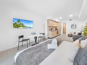 A modern living room with a sofa, a dining area with a table and chairs, a kitchen with wooden cabinets, and a large window with a tropical beach view. - Stunning Downtown Studio | Rooftop Pool | Skyline Views (Miami)