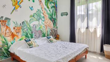 Une chambre à coucher avec un lit, une peinture murale représentant des animaux, une fenêtre avec des rideaux et une table de chevet avec une lampe.