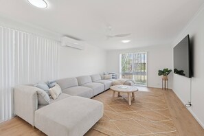 Un salon moderne avec un canapé d’angle, une table basse ronde et un téléviseur à écran plat fixé au mur.