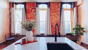 A kitchen with a marble countertop, a sink, a vase with flowers, and a brick wall. - American Hall Kaufman Suite (Millersburg)