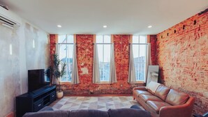 A living room with a brick wall, a leather sofa, a TV, and a potted plant. - American Hall Kaufman Suite (Millersburg)