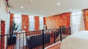 A modern hotel room with a brick wall, large windows, a balcony, and a bed. - American Hall Kaufman Suite (Millersburg)