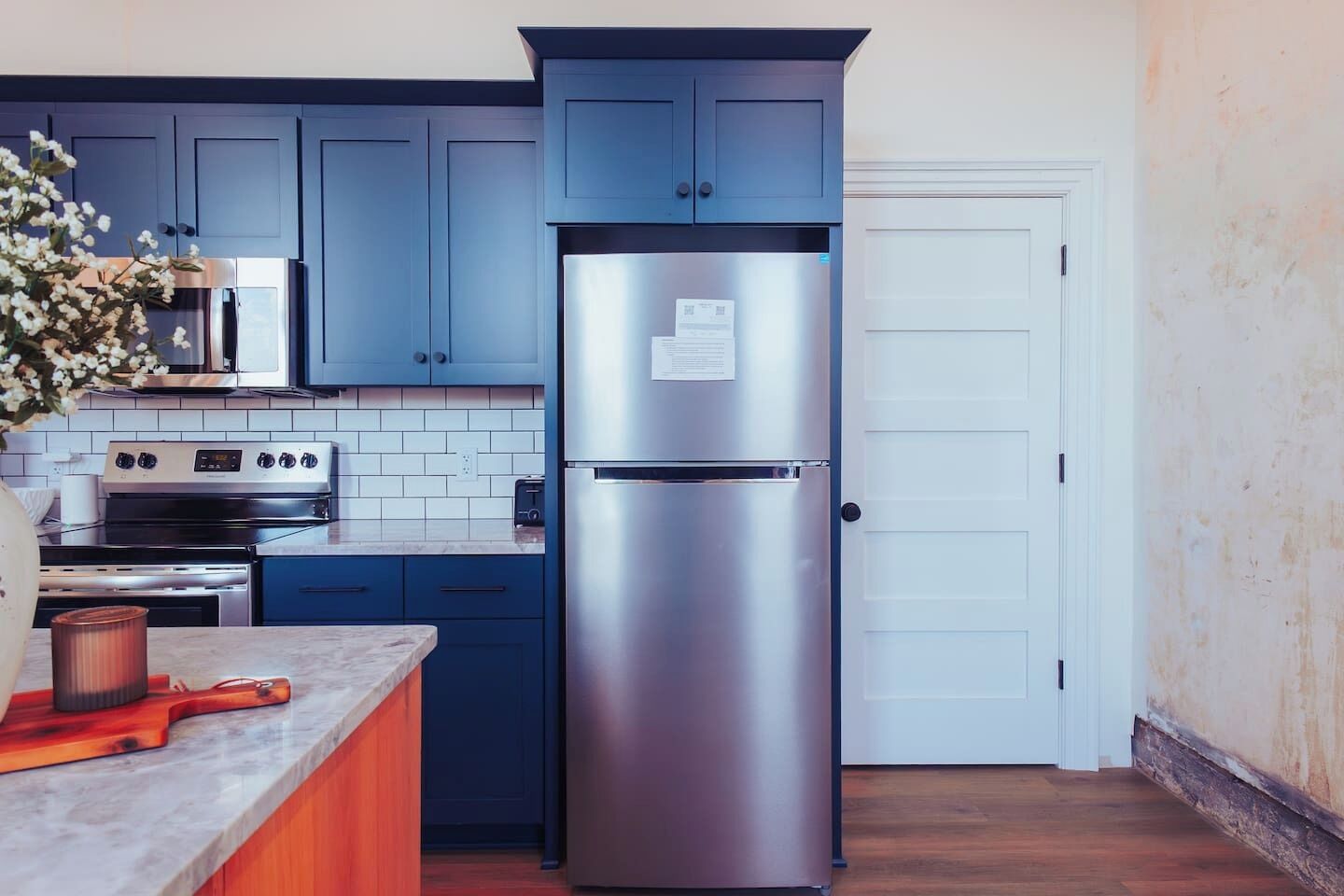 Una cocina con armarios azules, electrodomésticos de acero inoxidable, una puerta blanca y encimera de madera.