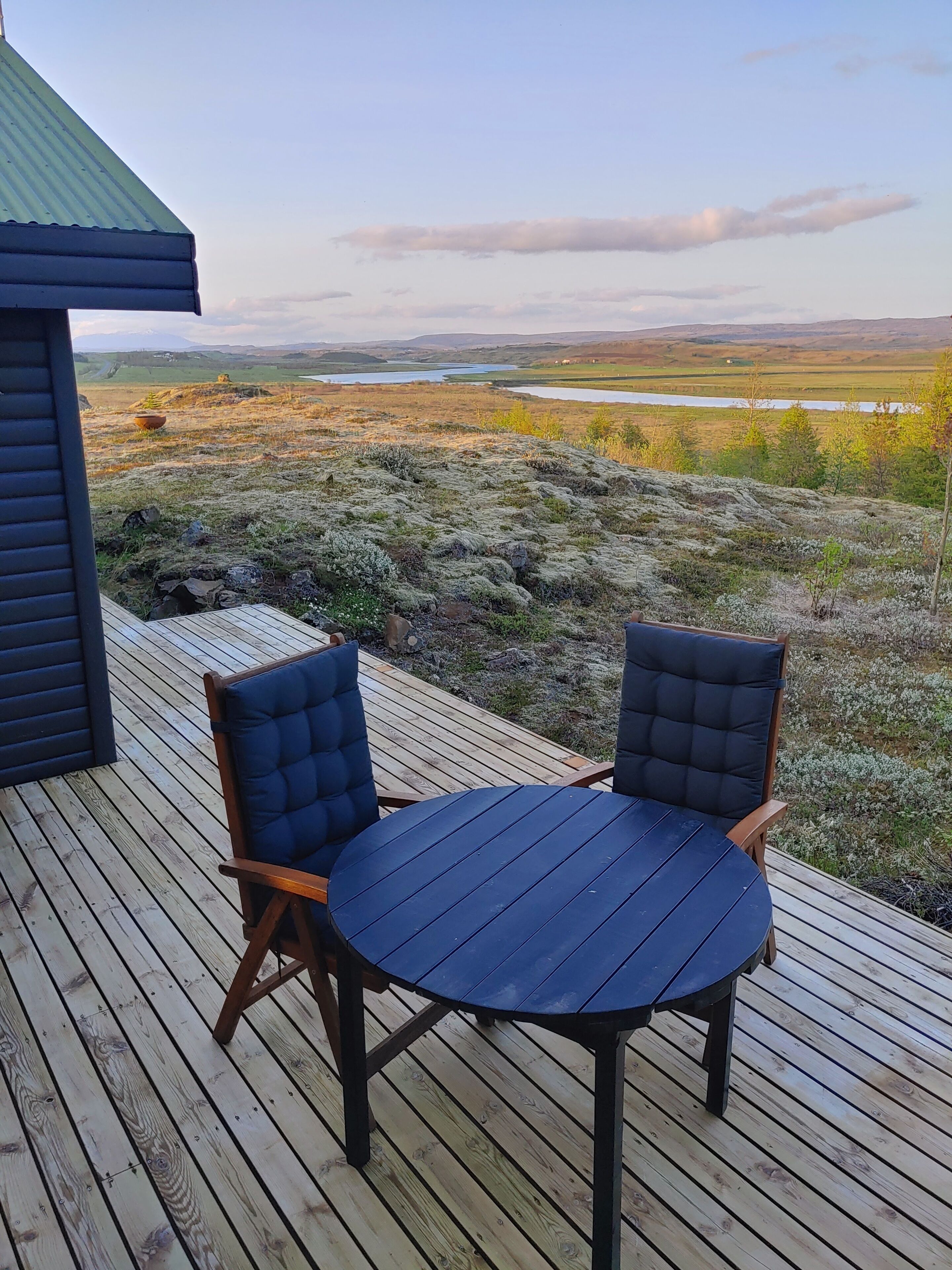 A deck with a table and two chairs, overlooking a landscape with hills and a body of water.
