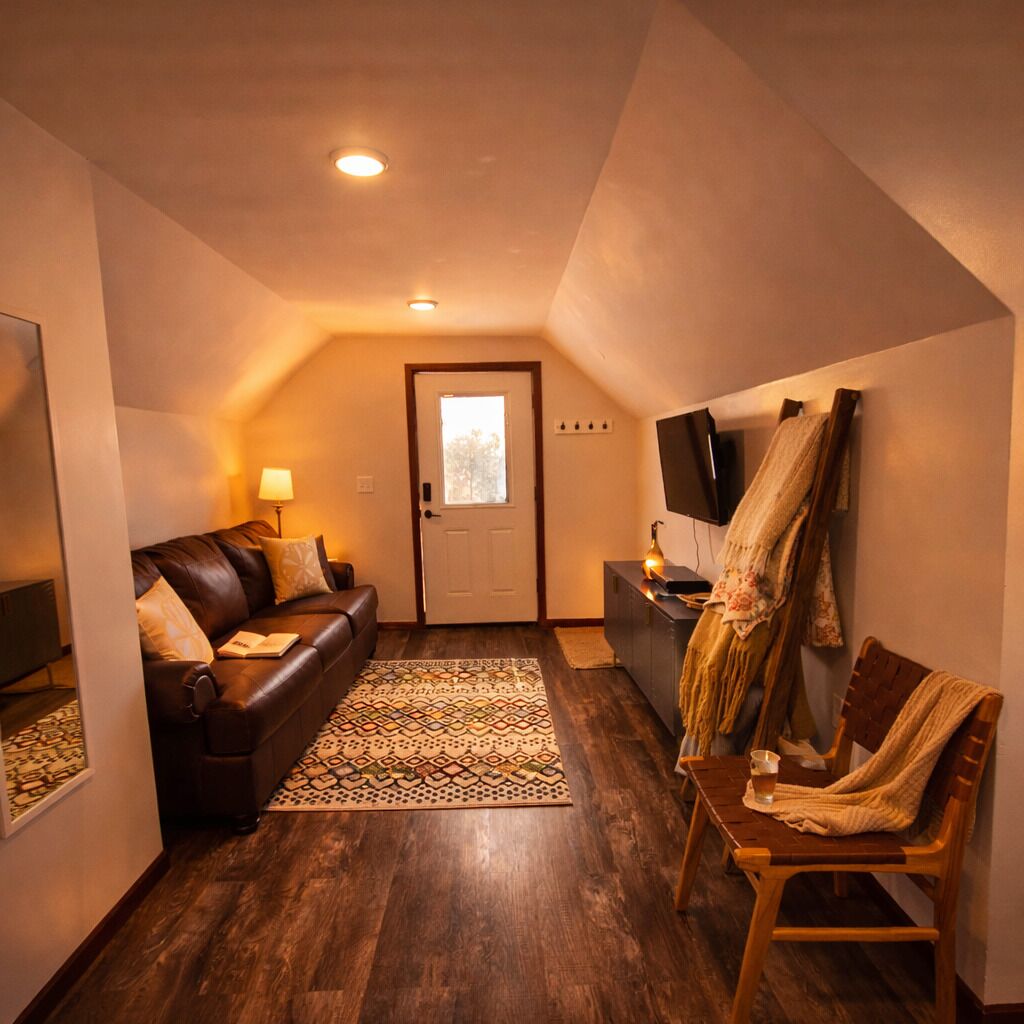 A cozy living room with a leather sofa, a wooden chair, a TV, and a patterned rug.