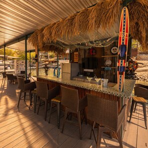 Eine Bar mit Korbstühlen, einem Reetdach, einer Surfbretthandlung und einem Schild, das auf Seeblick verweist.