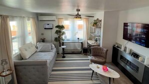 A modern living room with a sofa, a coffee table, a TV, and a ceiling fan. - Charming house in pleasant Yucca Valley (Yucca Valley)