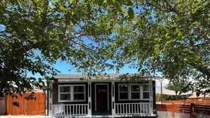 A small, two-story building with a porch, surrounded by trees and a gravel driveway. - Charming house in pleasant Yucca Valley (Yucca Valley)