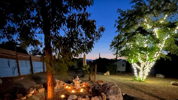 A nighttime outdoor setting with a wooden deck, rocks, and a tree with illuminated lights. - Charming house in pleasant Yucca Valley (Yucca Valley)