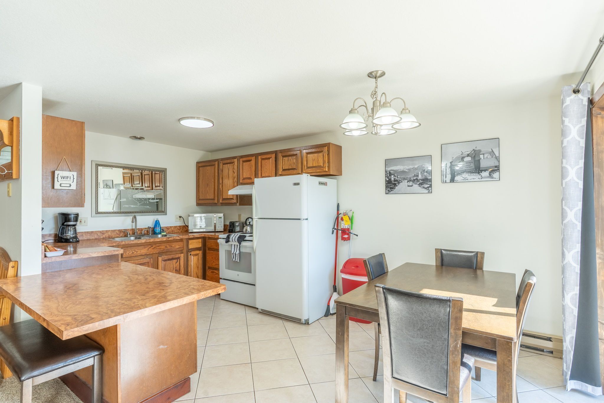 A kitchen with wooden cabinets, a refrigerator, a dining table with chairs, and a chandelier.