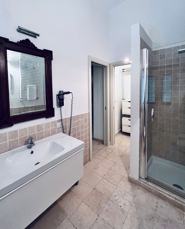 A bathroom with a large white sink, a mirror, a towel rack, and a shower area.
