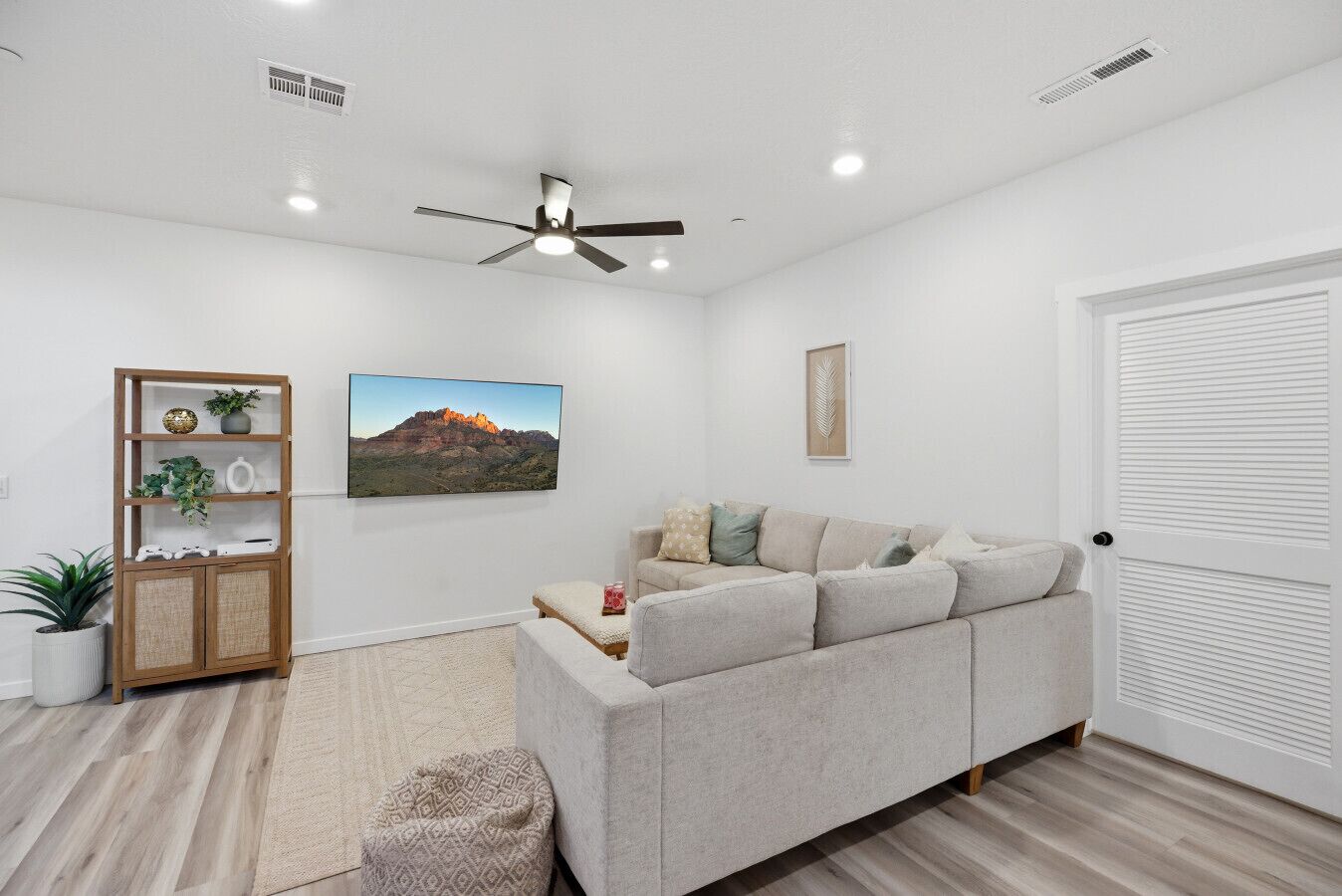 A living room with a sofa, a ceiling fan, a framed picture, a bookshelf, and a door.