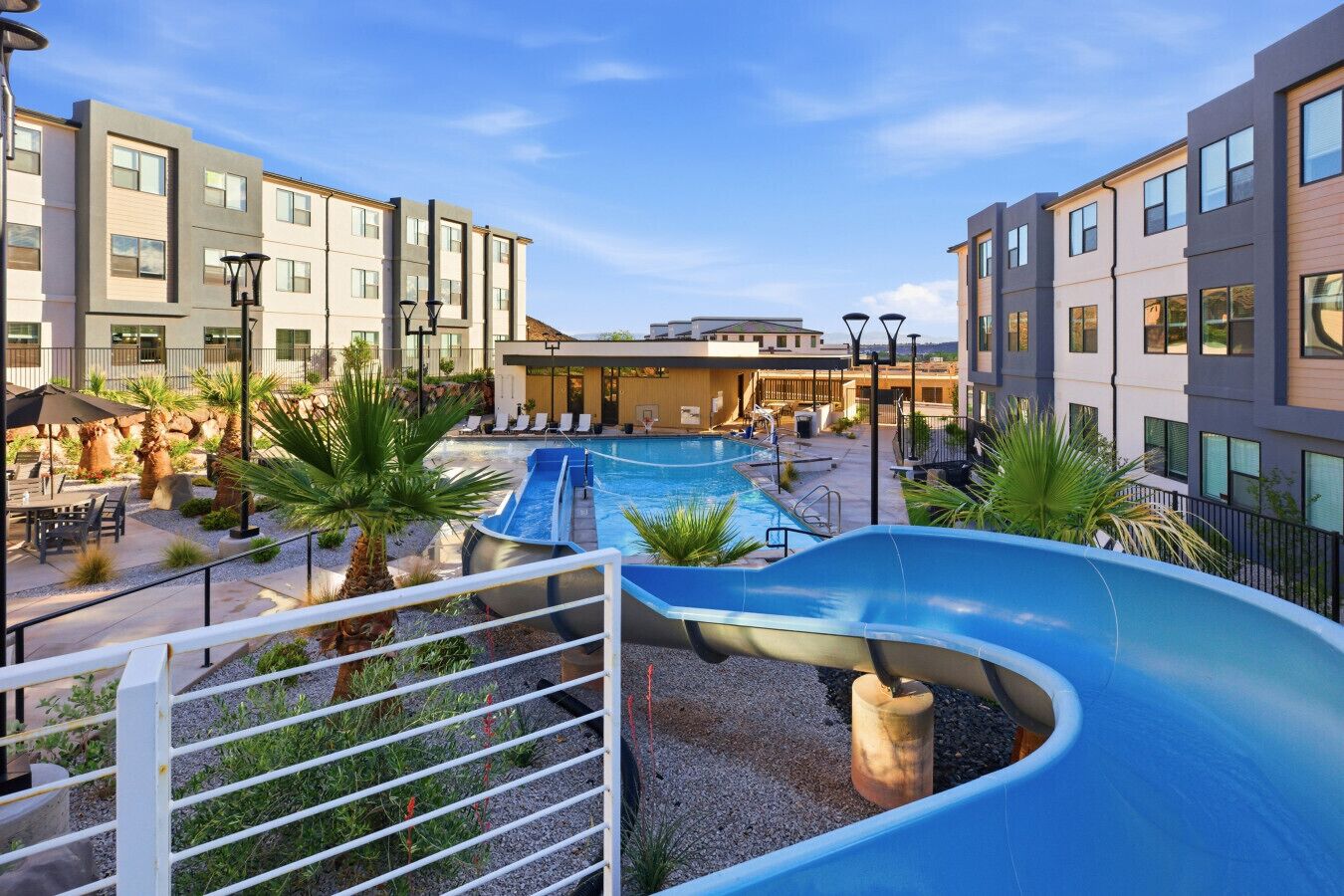 A pool area with a slide, lounge chairs, and a building with multiple floors.