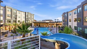 Un espace piscine avec un toboggan, des chaises longues et un bâtiment à plusieurs étages.