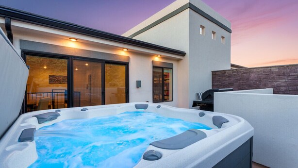 Un espace moderne aménagé à l’extérieur avec un jacuzzi, une porte d’entrée en verre, un mur en pierre et une terrasse dotée d’un barbecue.