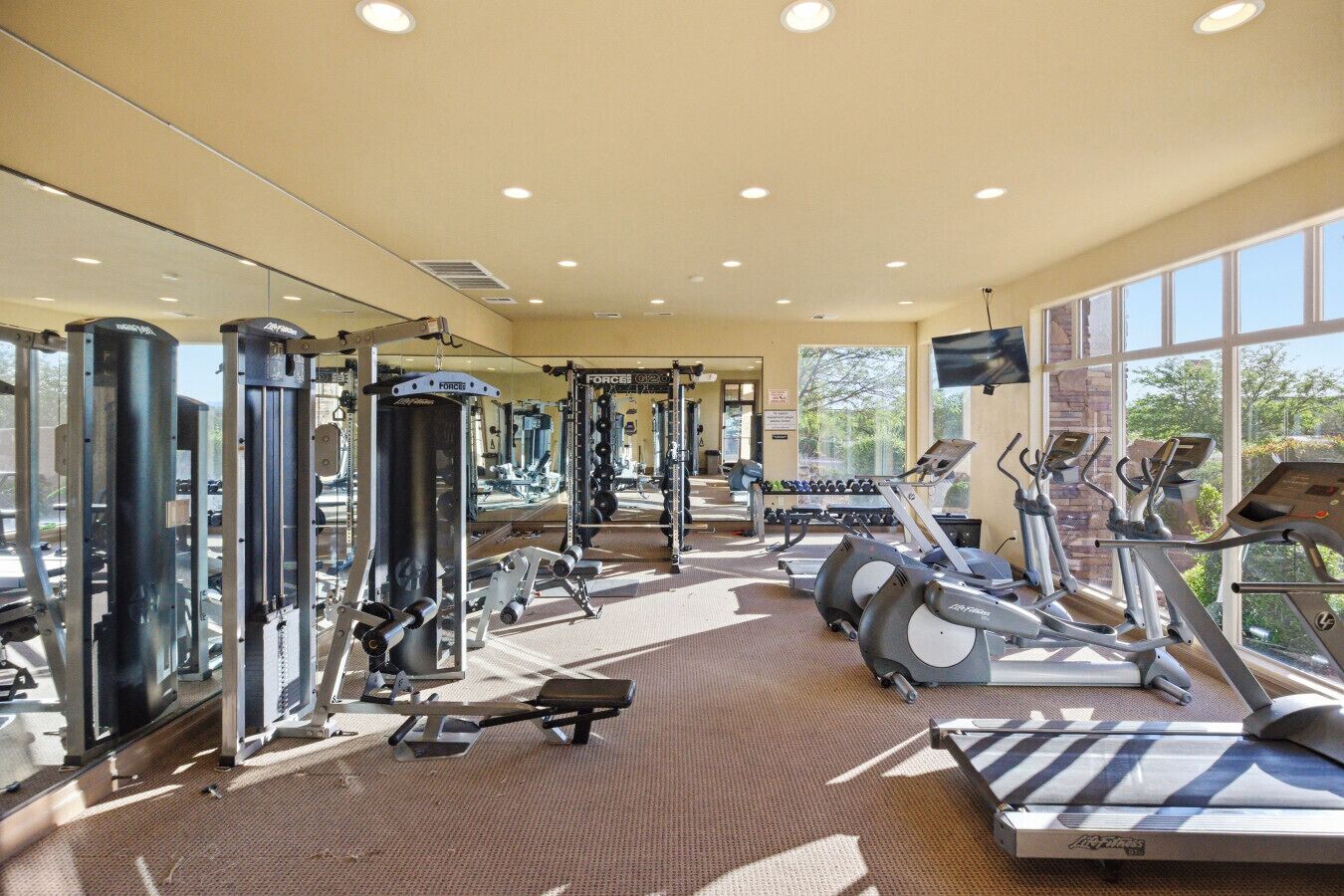 A gym with various exercise equipment, large windows, and a mirror.