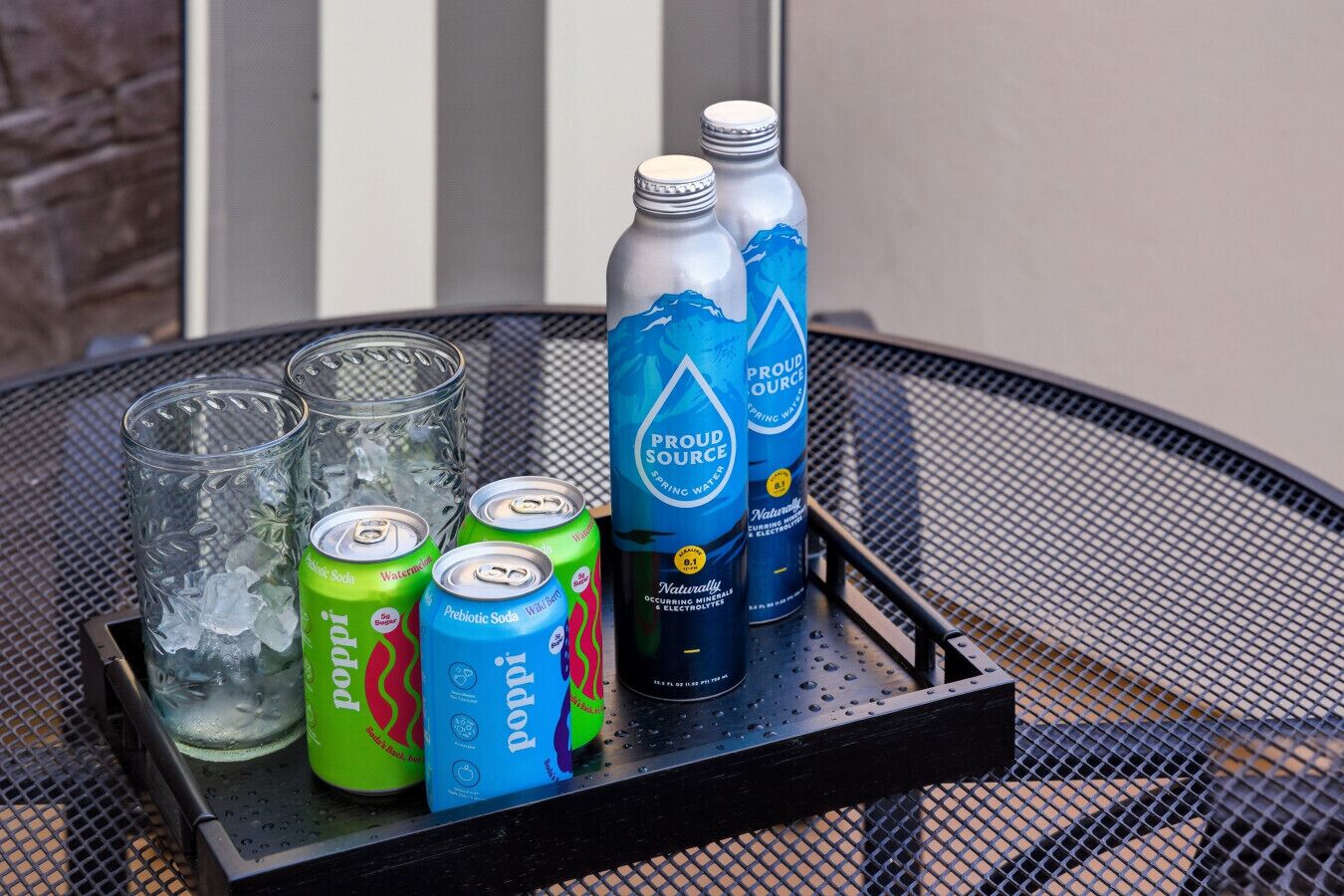 Un plateau en métal avec trois verres, deux canettes d’eau et deux bouteilles d’eau.