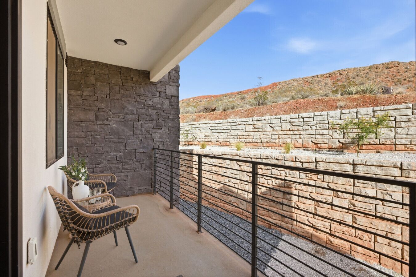 A balcony with stone walls, a wicker chair, and a view of a dry landscape.