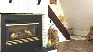 A fireplace with a black mantel, white brick wall, and a wooden floor.