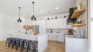 Una cocina moderna con armarios blancos, una isla de mármol y taburetes de bar.