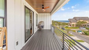 A balcony with a ceiling fan, a wicker chair, and a view of the ocean and neighboring houses. - Casa Blanca Sol Luxe Sea View House w Pool (Surfside Beach)
