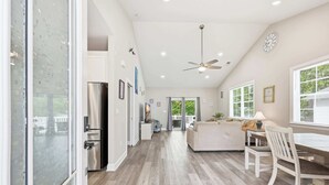 A spacious kitchen with a refrigerator, dining table, and chairs, leading to a living area with a sofa and a window. - Salty Seagull Pet Friendly Beach House (Myrtle Beach)