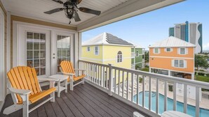 En inglasad veranda med två Adirondack-stolar, en takfläkt och utsikt över färgglada hus och en swimmingpool.