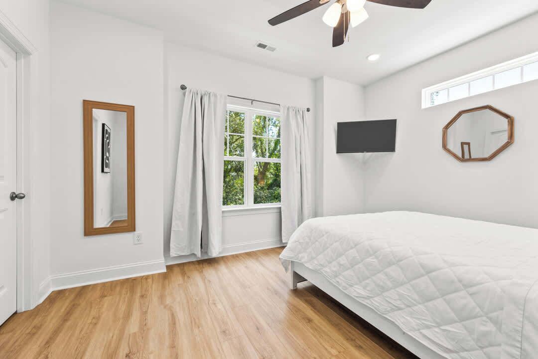 Un dormitorio con cama, ventilador de techo, ventana con cortinas, televisor y espejo.