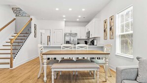A modern kitchen with white cabinetry, a wooden dining table, and a staircase with wooden railings.
