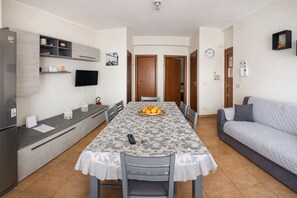 A compact living space with a dining table, sofa, kitchenette, and a TV mounted on the wall. - Angy's House (Terrasini)
