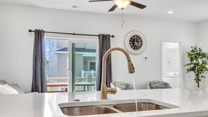 A modern kitchen with a stainless steel sink, a ceiling fan, and a view of the outside balcony. - Horizon Dune Pet Friendly House Walk to Beach (Myrtle Beach)