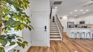 A modern kitchen with white cabinets, a wooden staircase, and a bar area with stools. - Horizon Dune Pet Friendly House Walk to Beach (Myrtle Beach)
