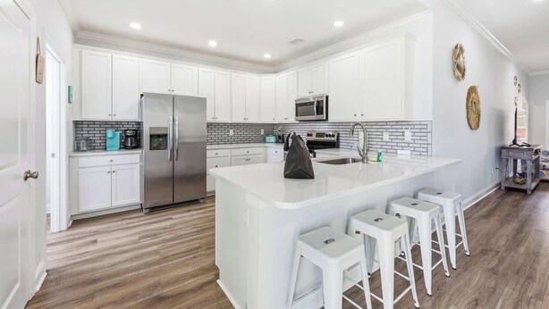 Una cocina moderna con armarios blancos, una isla central con taburetes, electrodomésticos de acero inoxidable y un salpicadero de azulejos.