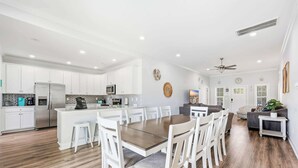 Una cocina moderna con armarios blancos, una isla central y un comedor con mesa de madera y sillas blancas.