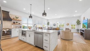 Une cuisine moderne dotée d’un îlot central, d’appareils électroménagers intégrés et de luminaires suspendus.