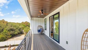 Un balcon doté d’un ventilateur de plafond, d’une chaise en osier et offrant une vue sur une zone boisée.