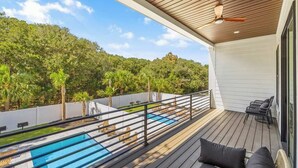 Une terrasse avec une piscine, du mobilier d’extérieur et une vue sur une colline boisée.
