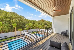 A deck with a pool, outdoor furniture, and a view of a forested hillside. - Casa Blanca Palace Luxe Sea View Home w 2 Pools (Surfside Beach)