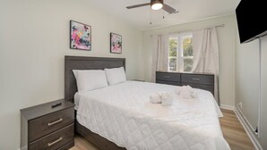 Un dormitorio con cama, mesita de noche, ventilador de techo y cuadros en la pared.