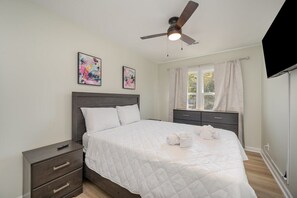 Une chambre à coucher avec un lit, une table de chevet, un ventilateur de plafond et des œuvres d’art accrochées au mur.
