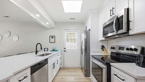 A modern kitchen with white cabinetry, a stainless steel refrigerator, a microwave, and a dishwasher. - Seabreeze Retreat Modern Home Walk to Beach (Myrtle Beach)