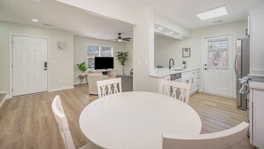 A spacious living room with a large white round table and matching chairs, a television, and a ceiling fan. - Seabreeze Retreat Modern Home Walk to Beach (Myrtle Beach)